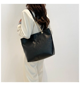 Detail of black crocodile pattern tote bag with gold chain strap on model's shoulder