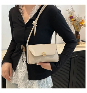 Detail of cream white baguette bag with gold metal buckle and knotted shoulder strap