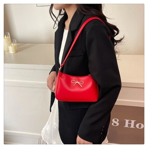 Detailed side view of a red shoulder bag featuring a decorative gold metal bow accent