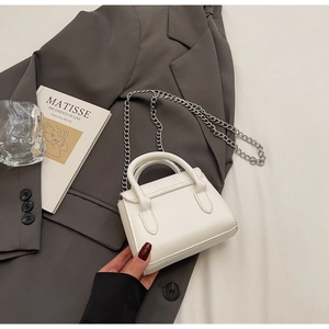 Detail of a white mini handbag with silver chain strap on a chic blazer background