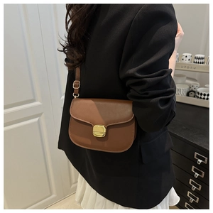Détail d'un sac bandoulière en cuir marron avec boucle métallique dorée rectangulaire fermée