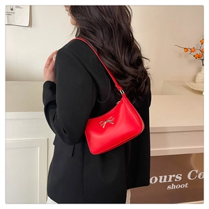 Detail of red hobo bag with gold bow clasp worn over a black blazer for a stylish look