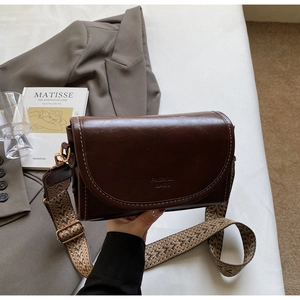 Detail of dark brown leather crossbody bag with white stitching and stylish wide strap