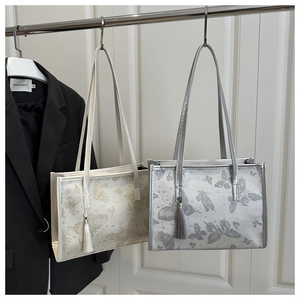 Detail of butterfly print tote bags in beige and silver with long fringe charms
