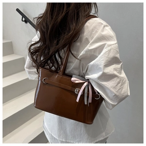 Detail einer dunkelbraunen Glanzhandtasche mit zarter Schleife und Schnalle