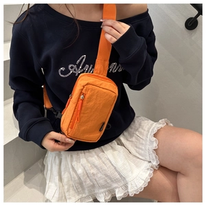 Orange waterproof mini crossbody bag with wide adjustable strap worn on blue sweatshirt