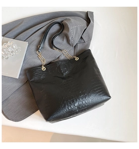 Detail of black faux crocodile skin texture on tote bag with golden metal chain strap