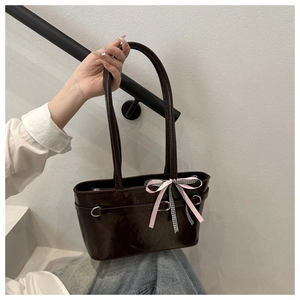Détail du sac à bandoulière marron brillant avec nœuds décoratifs roses et à carreaux