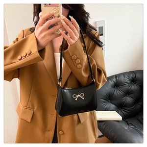Detail of black leather underarm bag with gold metal bow shown on model
