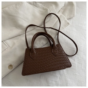 Detail of dark brown woven leather texture on a trapezoid handbag with dual handles