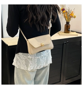 Model wearing a beige leather baguette bag with a stylish golden buckle in a home setting