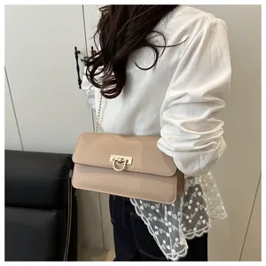 Détail d'un sac bandoulière beige avec boucle en D dorée, chaîne et rabat rectangulaire
