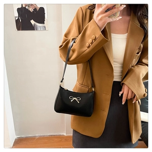 Close-up of black PU leather shoulder bag with a gold bow buckle on a model