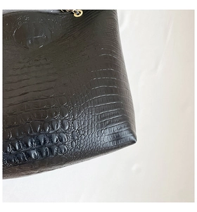 Close-up of black crocodile embossed leather texture with golden metal ring detail