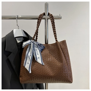 Detail of dark brown woven tote bag with braided handles and floral scarf decoration