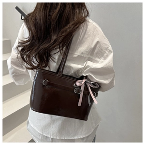 Détail du sac en cuir verni marron foncé avec un nœud en ruban à carreaux rose sur l'anse