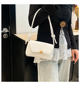 Detail of white leather baguette bag with gold metal clasp and knotted rope strap