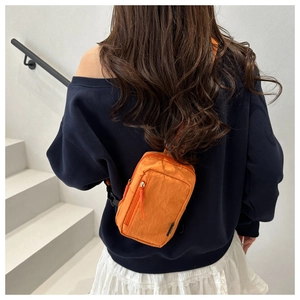 Detail of orange nylon chest bag with adjustable black strap and multi-zipper pockets