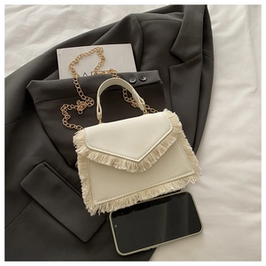 Detail of cream tassel crossbody bag with gold chain and fringe on minimalist background
