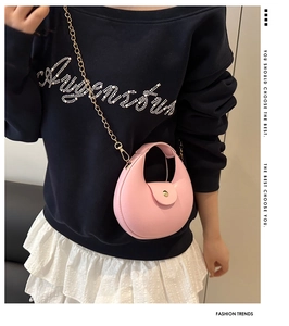 Sac bandoulière rond rose à chaîne dorée porté par un mannequin pour un style quotidien