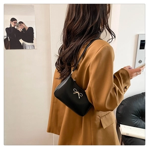 Detail of black faux leather baguette bag featuring a chic golden bow metal accent