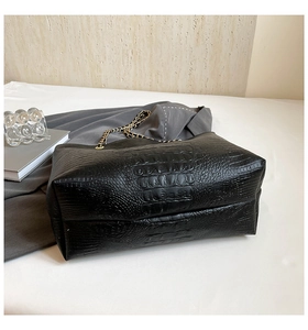 Detail of black crocodile embossed tote bag with gold chain strap on white fabric