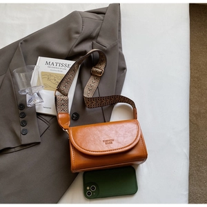 Detailed shot of retro brown crossbody bag with wide geometric patterned strap on blazer