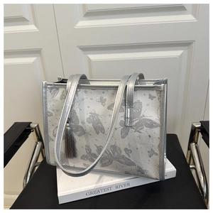 Close-up of silver tote bag featuring grey butterfly prints and fringe tassel detail