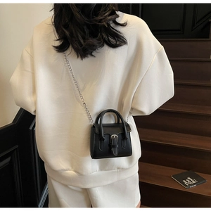 Detailed back view of a mini black leather handbag with silver chain on a white outfit