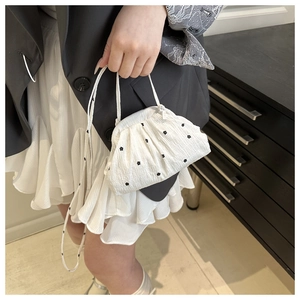 Detail of floral embroidery on white pleated handbag with delicate shoulder strap