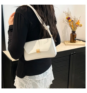 Close-up of white baguette bag with gold buckle and knotted strap on woman's shoulder