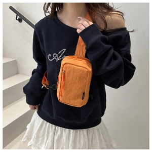 Detail of orange nylon crossbody bag with textured fabric and black buckle strap