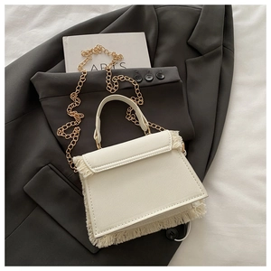 Close-up of white leather handbag with fringe details, gold chain, and flap closure