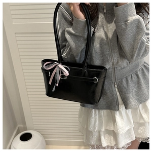 Detail einer schwarzen glänzenden Handtasche mit rosa Schleife und Metallring