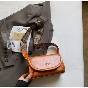 Caramel brown leather crossbody bag with ethnic woven strap displayed on a grey blazer