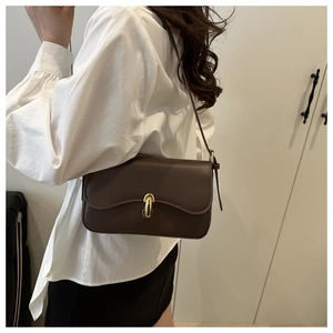 Detail of a dark brown leather shoulder bag with gold metal clasp and wavy flap design