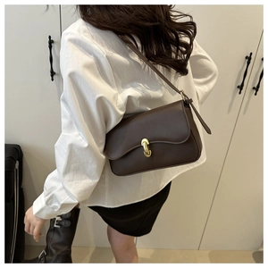 Detail view of a retro dark brown leather crossbody bag with a gold metal clasp on model