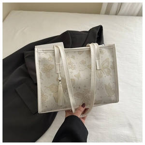 Detail view of white tote bag with golden butterfly print and elegant silk tassel