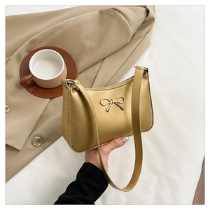 Detail of champagne gold crescent underarm bag with metal bow accent and smooth finish