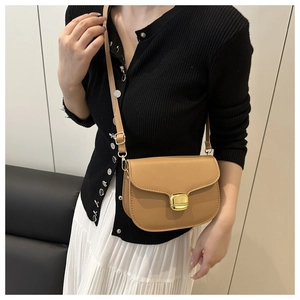 Détail du sac besace camel en cuir avec boucle dorée porté par le mannequin