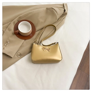 Detail of metallic gold baguette bag featuring a golden bow buckle on a beige blazer