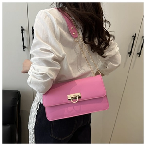 Detail of pink chain crossbody bag with golden buckle shown on shoulder of a model