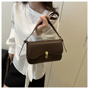 Detail showing the deep brown leather shoulder bag with a gold metal clasp on a white shirt