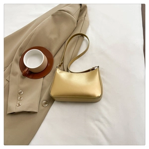 Chic metallic gold baguette bag with slender shoulder strap on white linen background