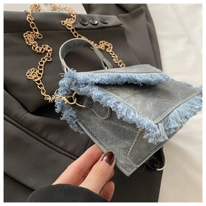 Detail view of denim mini crossbody bag with frayed fringe edges and gold chain strap