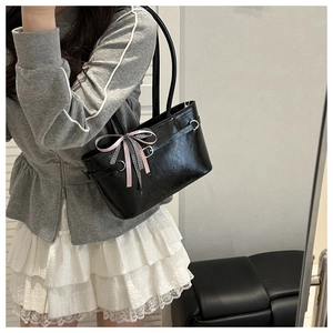 Detailansicht der schwarzen Lackleder-Tasche mit dekorativer rosa Schleife und Karomuster