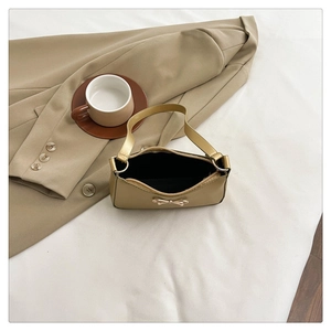 Detailed top view of beige shoulder bag featuring a decorative golden bow and zipper close