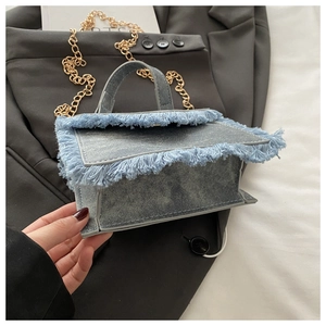 Detail of blue denim crossbody bag featuring long fringe edges and gold chain strap
