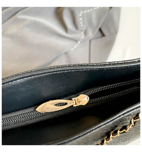 Macro detail of the gold leaf zipper pull and embossed leather texture on the black tote