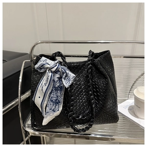 Detail of a black woven tote bag with a chain handle and a French printed silk scarf accessory
